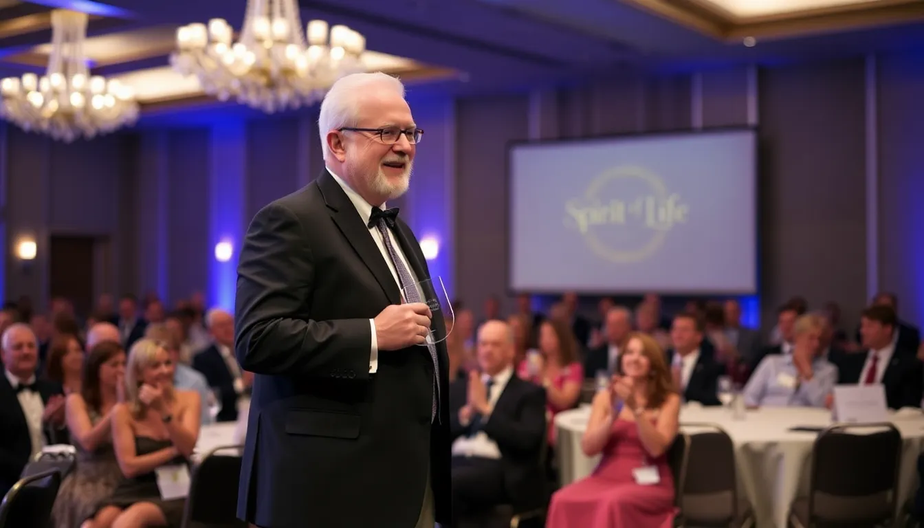 Larry Mestel stands on stage at the Spirit of Life gala, receiving an award while a crowd of attendees applauds in the background.