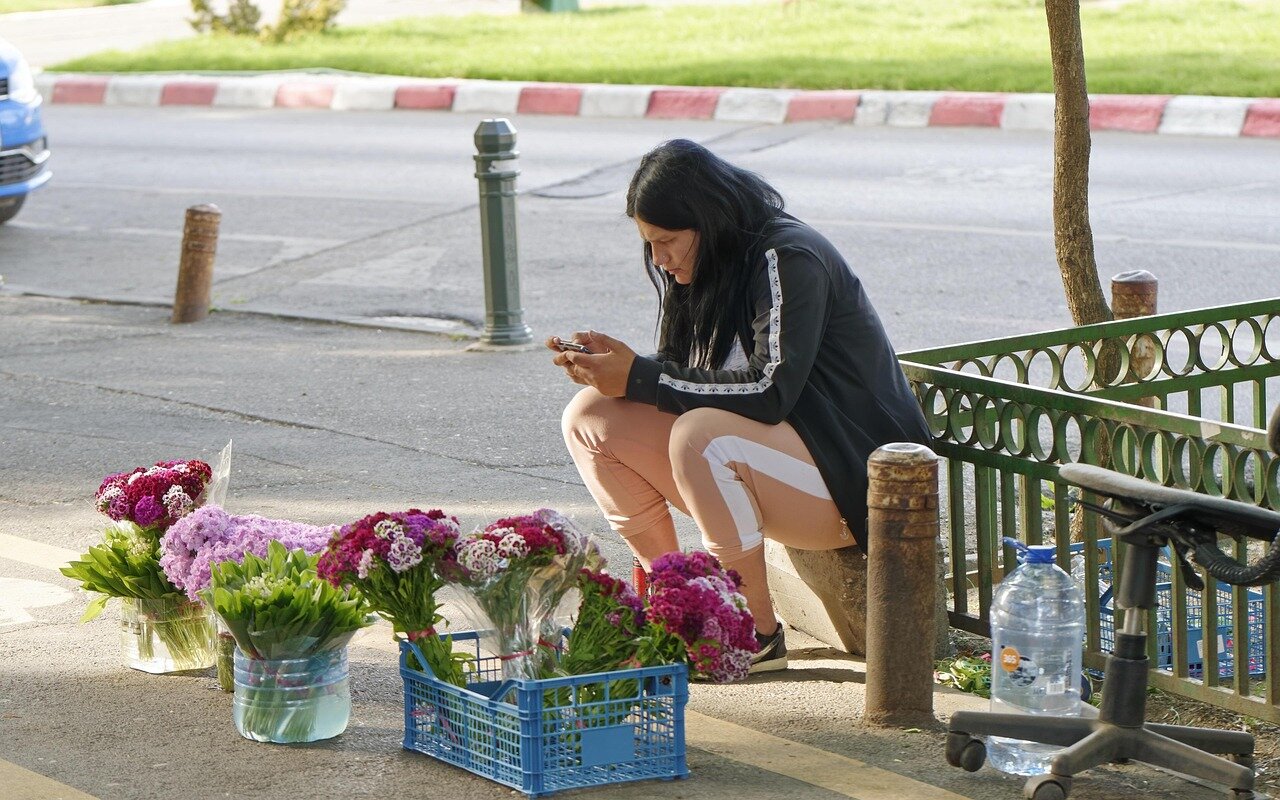 A celebrity assistant is seen managing a busy schedule on a tablet while standing next to a luxury car outside a highprofile event.