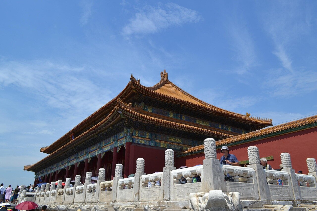 A group of officials in formal attire engages in a serious discussion outside the gates of Zhongnanhai, with the iconic architecture of the compound visible in the background.