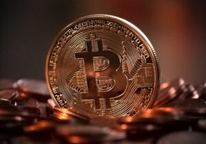 A group of diverse individuals gathers around a table, engaged in a discussion about cryptocurrency trends and terminology, with laptops and notepads in front of them.
