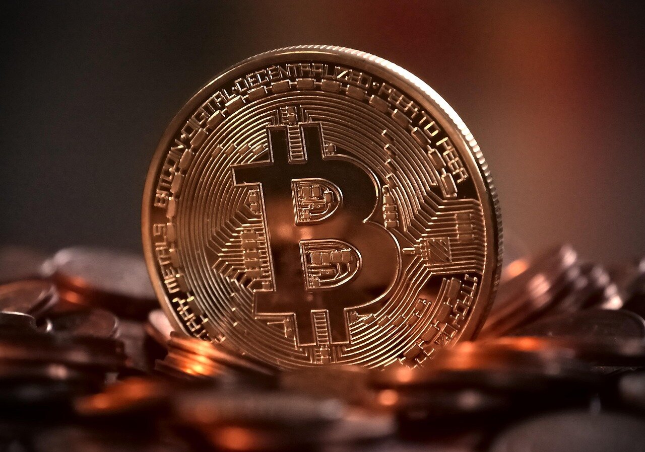 A group of diverse individuals gathers around a table, engaged in a discussion about cryptocurrency trends and terminology, with laptops and notepads in front of them.