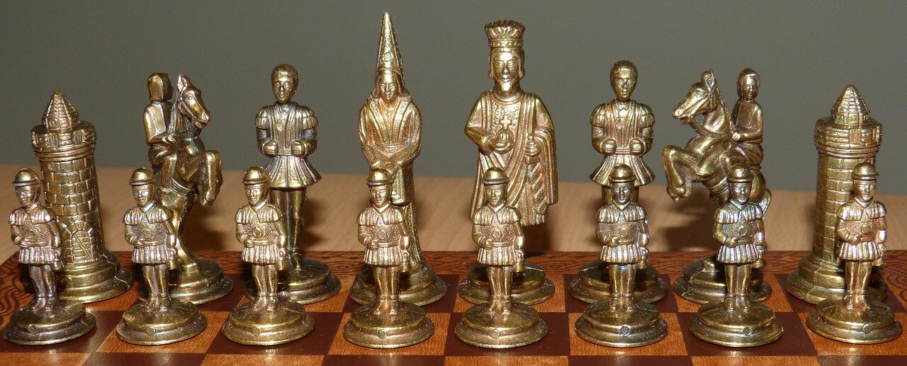 A group of chess enthusiasts gathers around a table, intently focused on solving a quirky chess puzzle displayed on a digital device, while colorful chess pieces are scattered around them.
