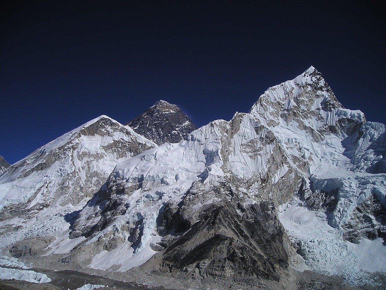 A mountaineering guide sits on a snowy ledge on Mount Everest, surrounded by towering ice formations, as he holds a chocolate bar in one hand and collects ice with the other, showcasing his resourcefulness during a sixday survival ordeal.
