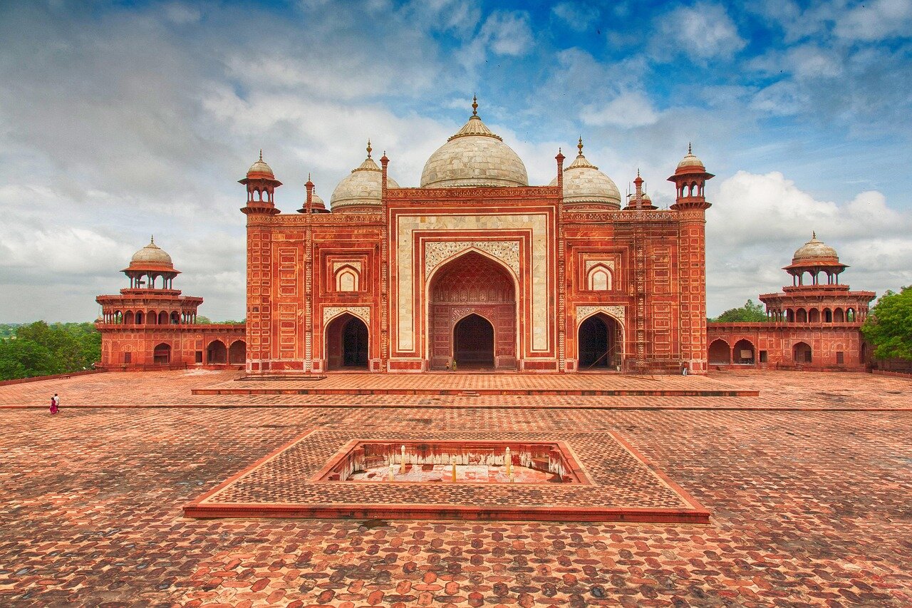 A bustling marketplace in Mughal India showcases traders and customers engaged in lively exchanges, surrounded by colorful textiles and spices.