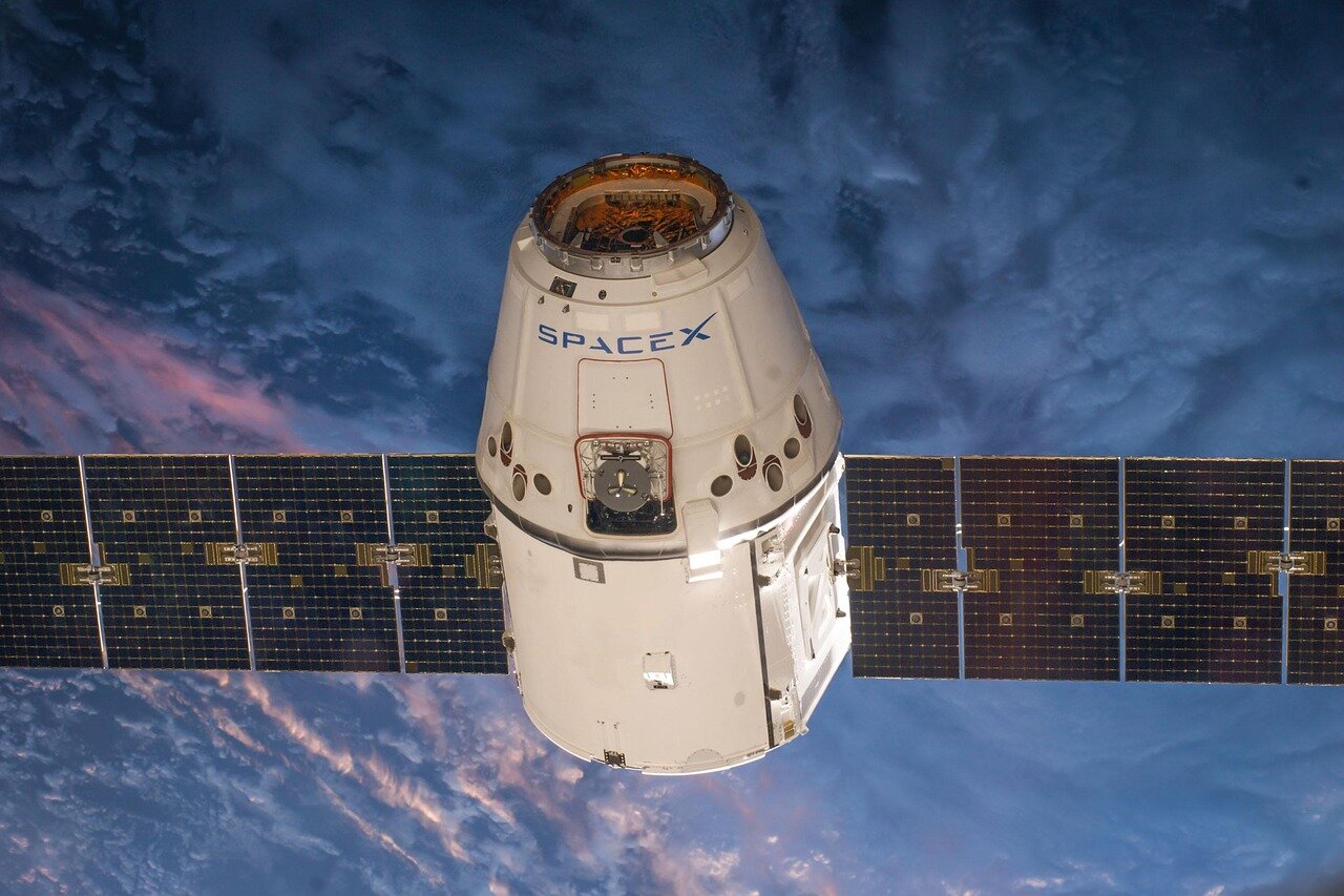 A SpaceX cofounder speaks at a press conference, highlighting the significance of the company's upcoming market debut while surrounded by models of rockets and satellite technology.