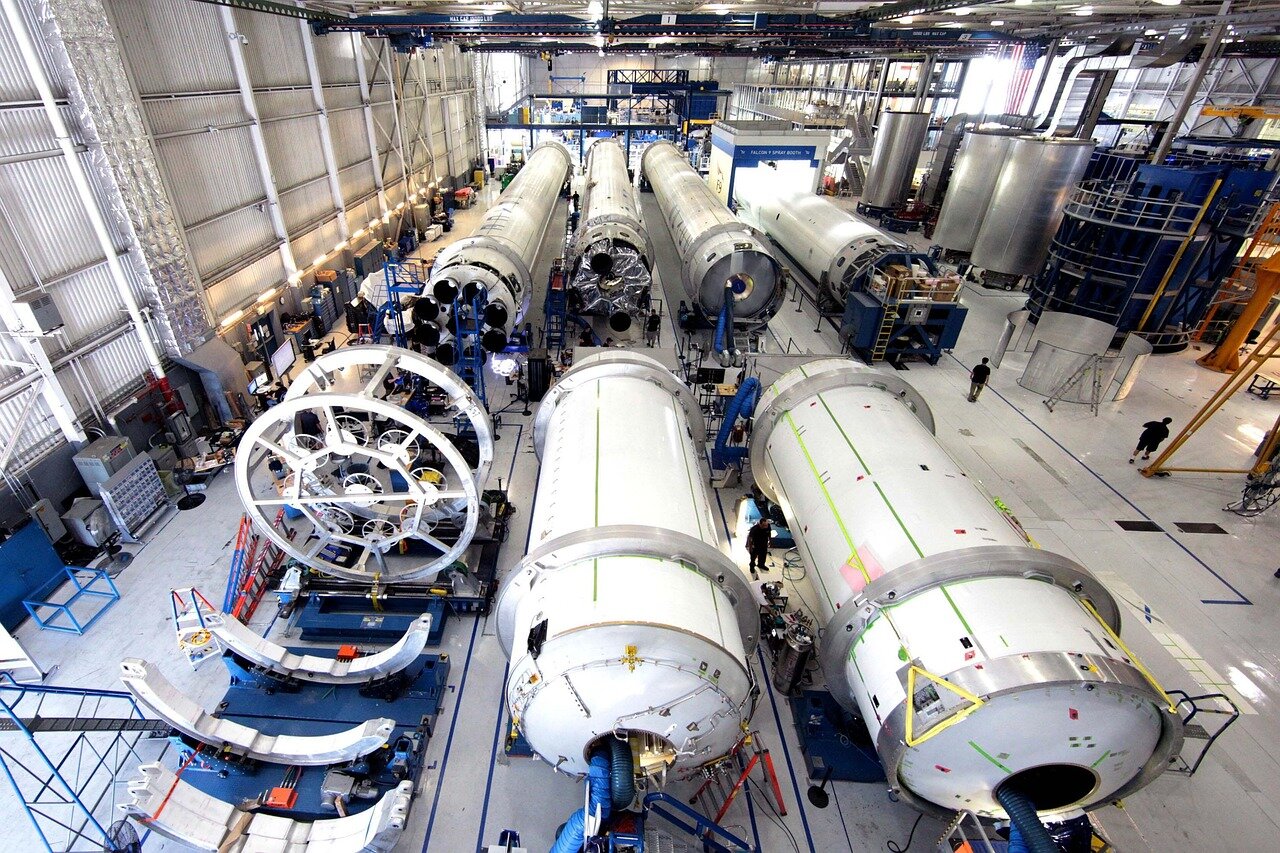 A group of SpaceX employees gathers in an office setting, discussing the recent inclusion of SpaceX stock in their 401(k) plans, with charts and financial documents spread out on the table.
