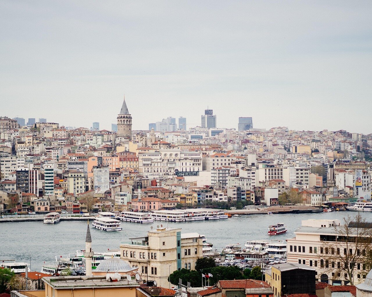 A large cruise ship is anchored off the coast, with a crowd of passengers visibly upset as they gather on the deck, while Turkish authorities enforce a blockade in the background.